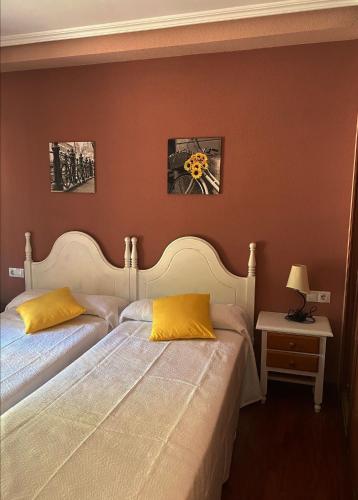Albergue Buen Camino في نافاريتيه: سريرين مع وسائد صفراء في غرفة النوم