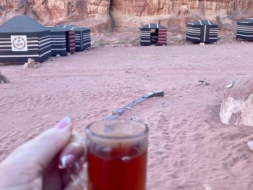 a person holding a glass of drink in the desert at Wadi Rum Moon Light Camp in Wadi Rum