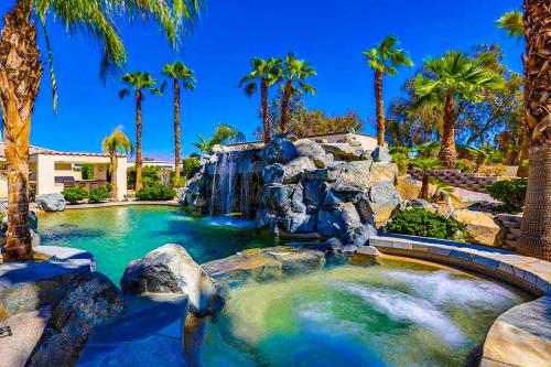 a pool with a waterfall in a backyard with palm trees at Cool Pool Retreat in Bermuda Dunes