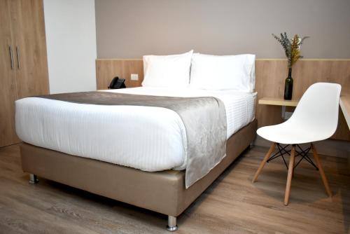 a bedroom with a large bed and a white chair at ExpoStay Hotel Corferias Embajada Americana in Bogotá