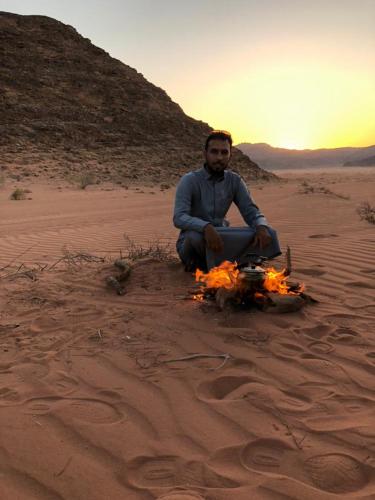 a man sitting in the desert with a fire at RUM STARDUST lUXURY CAMP in Wadi Rum