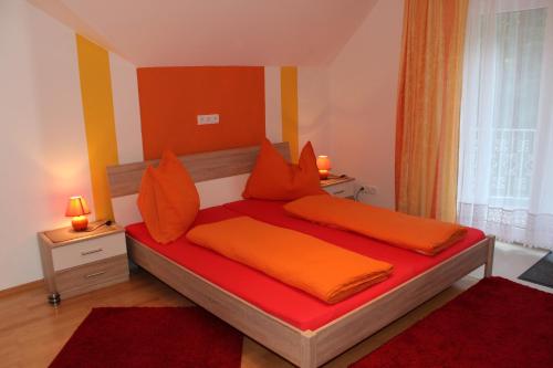 Schlafzimmer mit einem Bett mit orangefarbener Bettwäsche und orangefarbenen Kissen in der Unterkunft Ferienwohnung am Wörthersee Villa Waldbach in Krumpendorf am Wörthersee