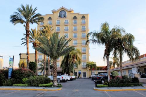 ein großes gelbes Gebäude mit Palmen auf einem Parkplatz in der Unterkunft Best Western Hotel Posada Del Rio Express in Torreón