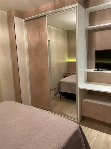 a bedroom with a mirror and a bed and a television at Apartamento em Gramado com piscina in Gramado