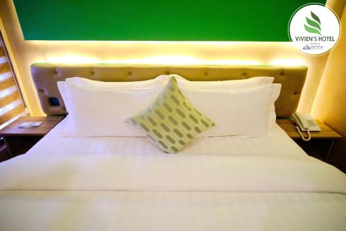a white bed with white pillows and a green wall at Vivien's Hotel in Mactan