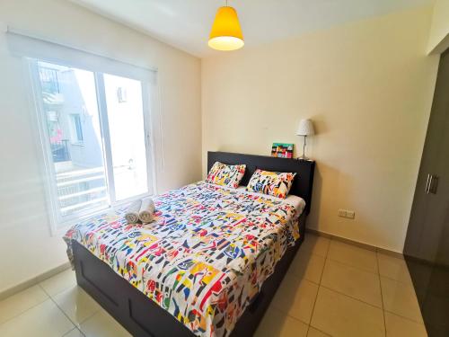 ein Schlafzimmer mit einem Bett mit einer Bettdecke und einem Fenster in der Unterkunft Promenade Breeze City Apartment in Larnaka