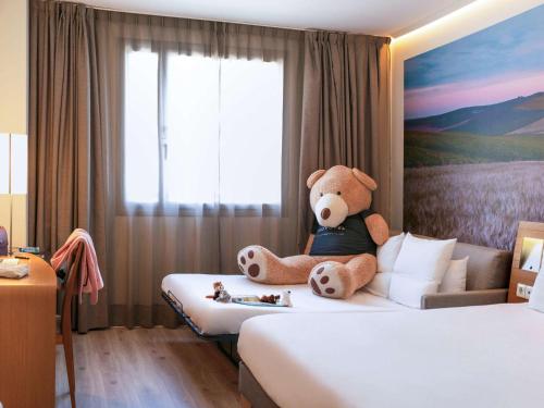 a teddy bear sitting on a bed in a hotel room at Hotel Novotel Sevilla in Seville