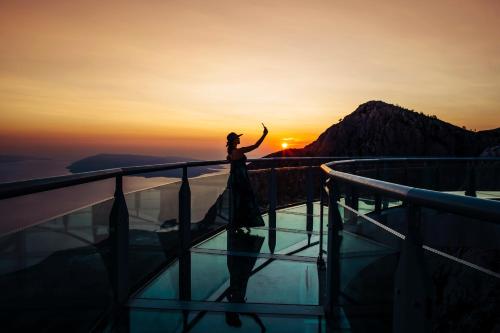 a woman standing on the edge of a viewing deck at sunset at Medora Orbis Mobile Homes & Glamping in Podgora