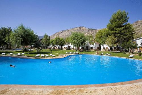 a large blue swimming pool with lounge chairs and trees at Complejo Residencial Los Enebros in Arroyo Frio