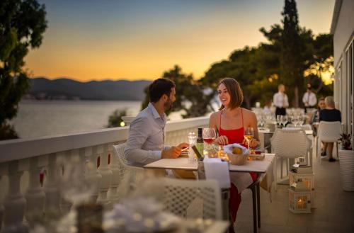 a man and woman sitting at a table with wine glasses at Aminess Younique Bellevue Hotel in Orebić