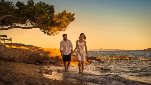 a man and woman walking on the beach at sunset at Aminess Younique Bellevue Hotel in Orebić