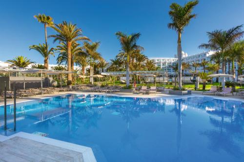 a large pool with palm trees and a hotel in the background at Hotel Riu Palace Maspalomas - Adults Only in Maspalomas