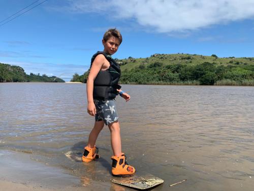 a young boy standing on a surfboard in the water at Umtamvuna River Lodge in Port Edward