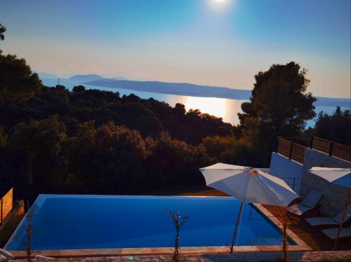 a pool with an umbrella and a view of the water at Damari Luxury Retreat Villas Skiathos in Skiathos Town