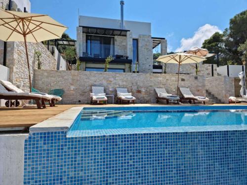 a swimming pool with chairs and umbrellas next to a house at Damari Luxury Retreat Villas Skiathos in Skiathos Town