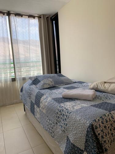 a bedroom with a bed with a blue blanket and a window at Magnolia apart Con facturas in Iquique