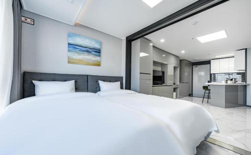 a bedroom with a large white bed and a kitchen at Songjeong Blue Castle Hotel in Busan
