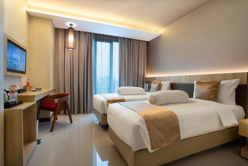 a hotel room with two beds and a desk at Braling Grand Hotel Purbalingga, Azana Hotels Collection in Purbolinggo