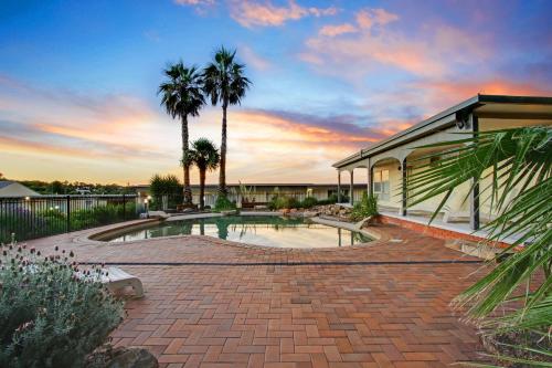 een zwembad met palmbomen en een huis bij Thunderbird Motel Yass in Yass