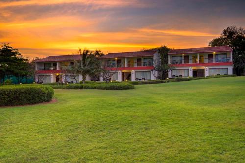 a building with a green yard in front of a sunset at Radisson Blu Resort Temple Bay Mamallapuram in Mahabalipuram