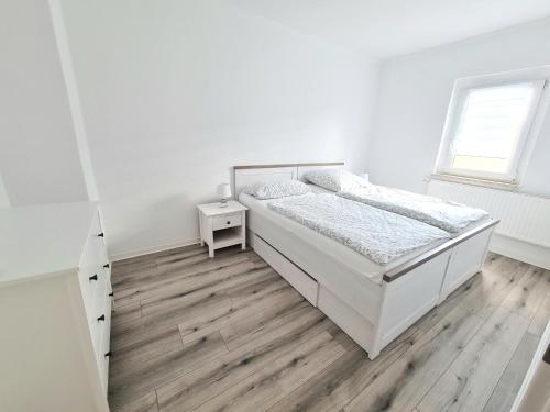 a white bedroom with a bed and a wooden floor at Ferienwohnung zur Burg in Crölpa