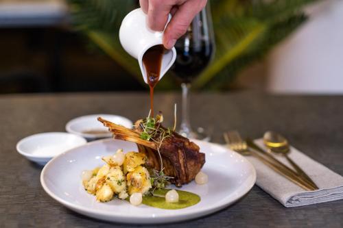 a person pouring sauce onto a plate of food at Rydges Armidale in Armidale