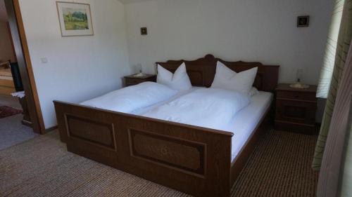 a large wooden bed with white sheets and pillows at Gästehaus Buchinger in Bayerisch Eisenstein