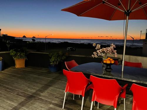 a table with red chairs and an umbrella on a deck at Ocean Front East End Beach House in New Plymouth