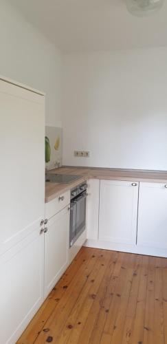 a kitchen with white cabinets and a wooden floor at Ferienhaus Am Heidebad in Schmelz