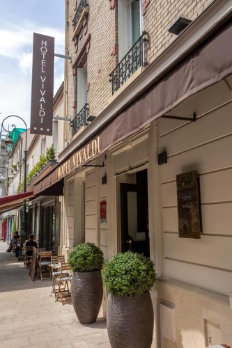 a building with two large pots of plants on a street at Hotel Vivaldi in Puteaux