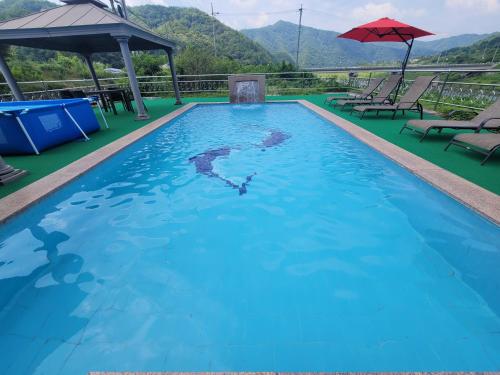 uma piscina com água azul e cadeiras e um guarda-sol em Tomato Pension em Hongcheon