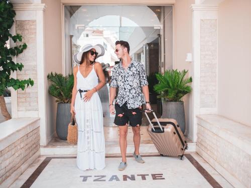 a man and a woman standing outside a building with a suitcase at Tzante Hotel Zakynthos, Adults Only in Laganas