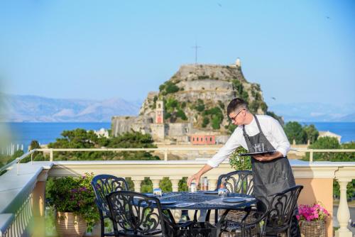 
a man sitting at a table in front of a balcony at Arcadion Hotel in Corfu
