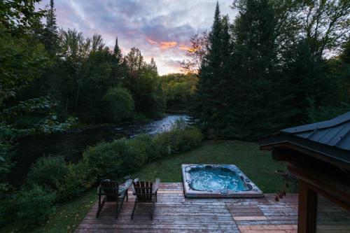 a backyard with a hot tub and chairs next to a river at The Beaver Lodge by Escapades Tremblant in Lac-Superieur