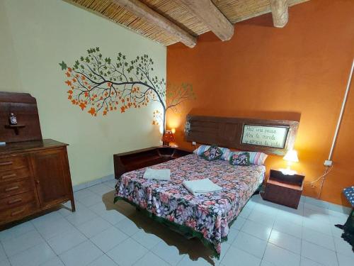 ein Schlafzimmer mit einem Bett und einem Baumbild an der Wand in der Unterkunft Munay EcoHostal - Cabañas de Adobe in Tinogasta