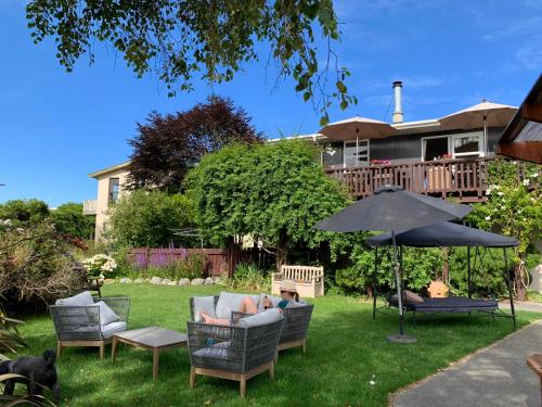 a man sitting in a chair under an umbrella in a yard at Brook House B&B & Cottages in Kaikoura