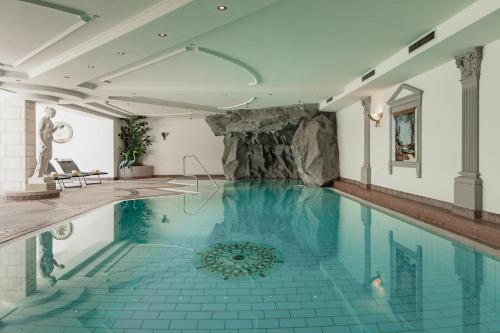 an indoor swimming pool with blue tile floors and a stone wall at Hotel Salzburg in Saalbach Hinterglemm
