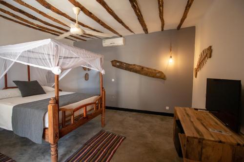a bedroom with a canopy bed and a tv at Nest Style Beach Hotel Zanzibar in Makunduchi