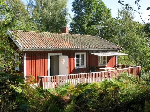 a red cottage with a deck in the woods at Holiday Home Järnemåla Margaretetorp by Interhome in Valdemarsvik