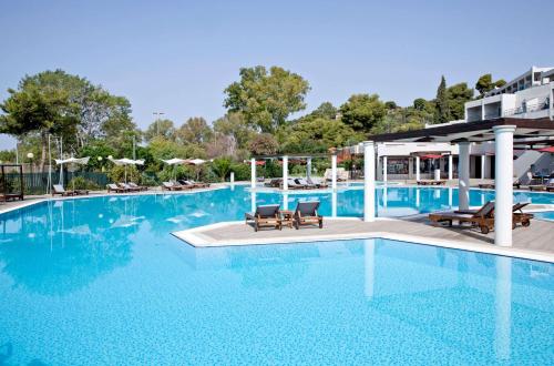 a large swimming pool with two chairs and a building at Dolce by Wyndham Athens Attica Riviera in Vravrona