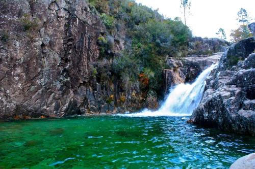 a waterfall in front of a mountain with green water at Casa do Charco Peneda Gerês in Parada