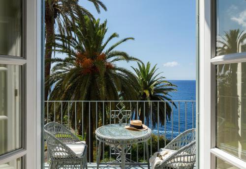 a table and chairs on a balcony with the ocean at Reid's Palace, A Belmond Hotel, Madeira in Funchal