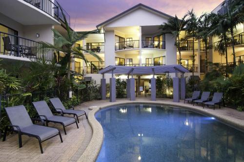 a hotel with a pool and chairs and a building at Bay Villas Resort in Port Douglas