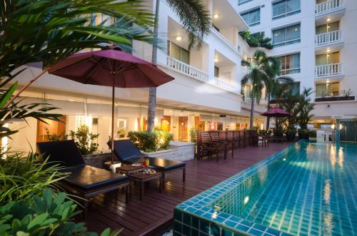 an outdoor pool with chairs and an umbrella and a hotel at AT EASE saladaeng by AETAS in Bangkok