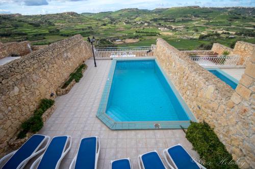 uma piscina exterior com cadeiras e uma parede de pedra em Orchidea Xaghra em Il-Pergla