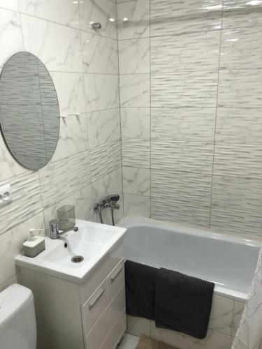 a white bathroom with a sink and a tub and a mirror at Квартира-студия в центре с балконом с белым постельным, рядом с Dostyk Mall in Petropavlovsk
