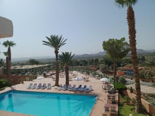 uma vista para uma piscina com cadeiras e palmeiras em Kenzi Azghor em Uarzazate