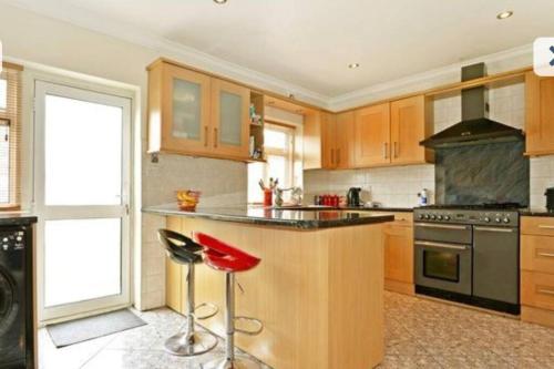 una cocina con armarios de madera y taburetes rojos en Beautiful 6 Bedroom with spacious Lounge & Rooms Free parking, en Erith