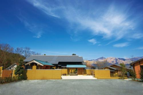 a house with a yellow fence and mountains in the background at Bettei Soan in Minami Aso