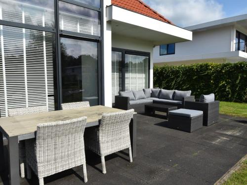 eine Terrasse mit einem Tisch, Stühlen und einem Sofa in der Unterkunft Holiday Home in Zeewolde with Jetty next to golf course in Zeewolde